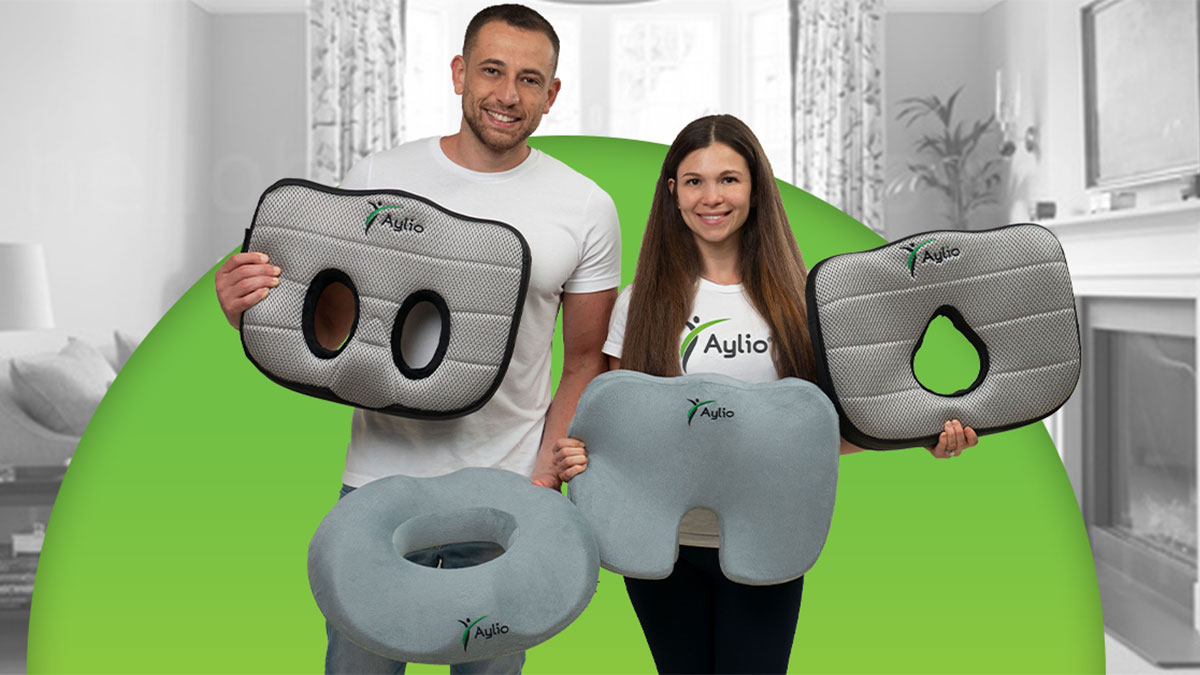 Max Krishtul and Larisa holding four Aylio cushions: a twin-opening seat cushion, a contoured center-opening cushion, a ring cushion, and a coccyx pillow.